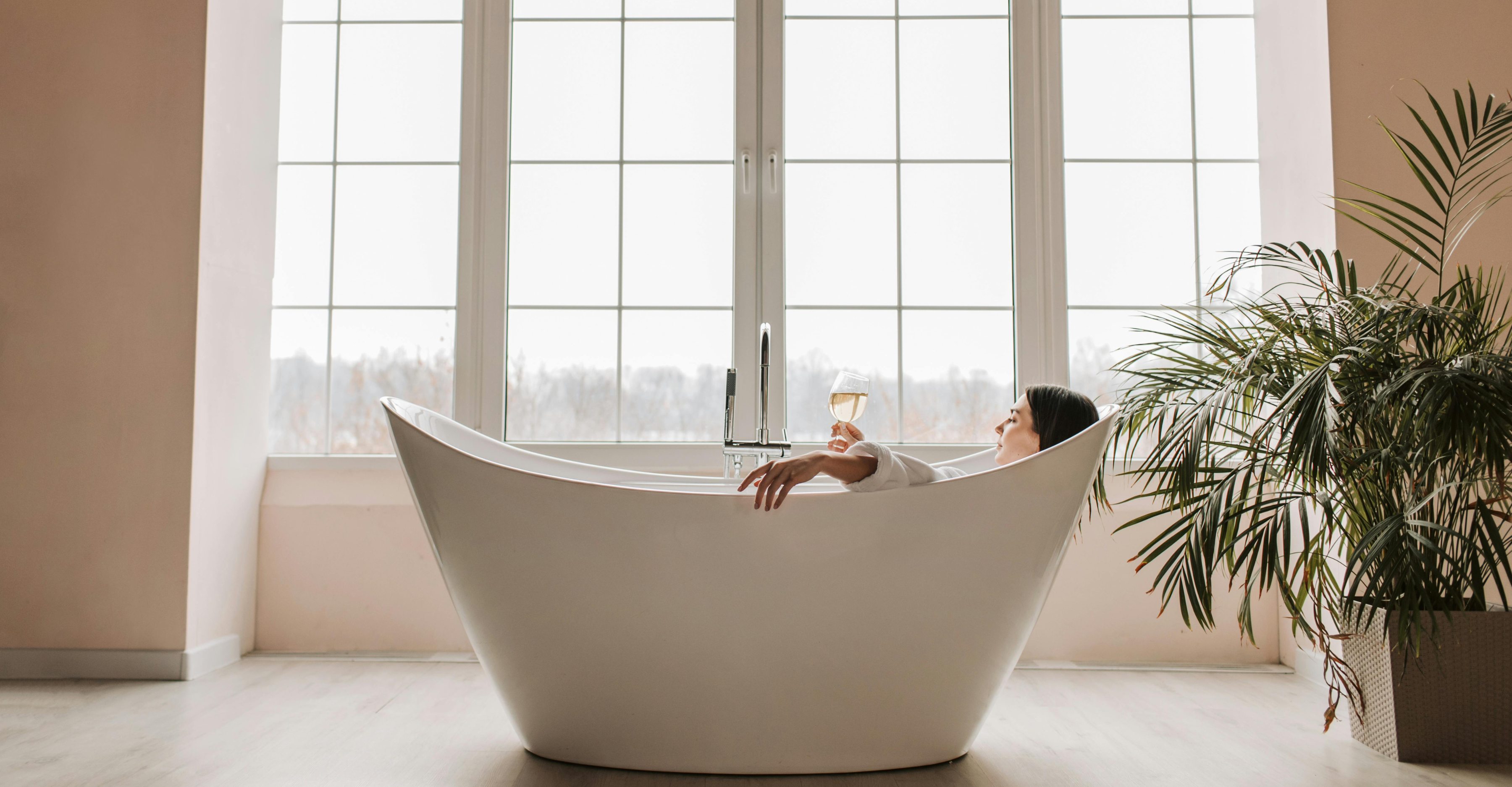 Person relaxing in a freestanding bathtub with a view of large windows.slider_item_YYkYAm